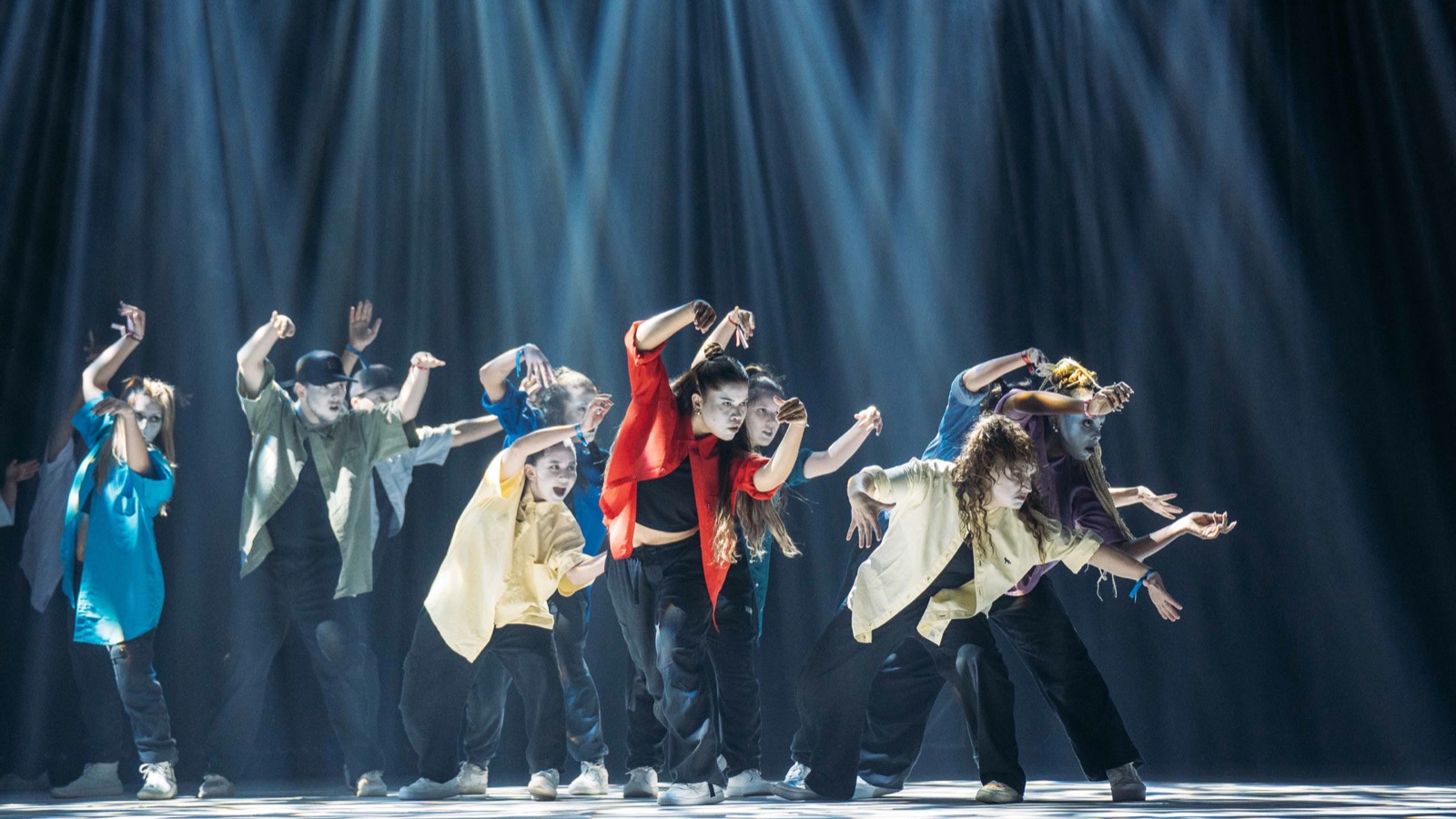 Apresentação no palco durante a mostra competitiva do Hip Hop District. Dançarinos em destaque sob iluminação dramática com luzes azuis e vermelhas, criando uma atmosfera intensa no palco.