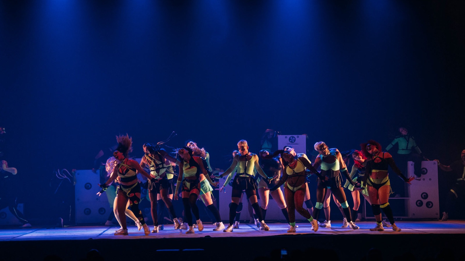 Apresentação no palco durante a mostra competitiva do Hip Hop District. Dançarinos em destaque sob iluminação dramática com luzes azuis e vermelhas, criando uma atmosfera intensa no palco.